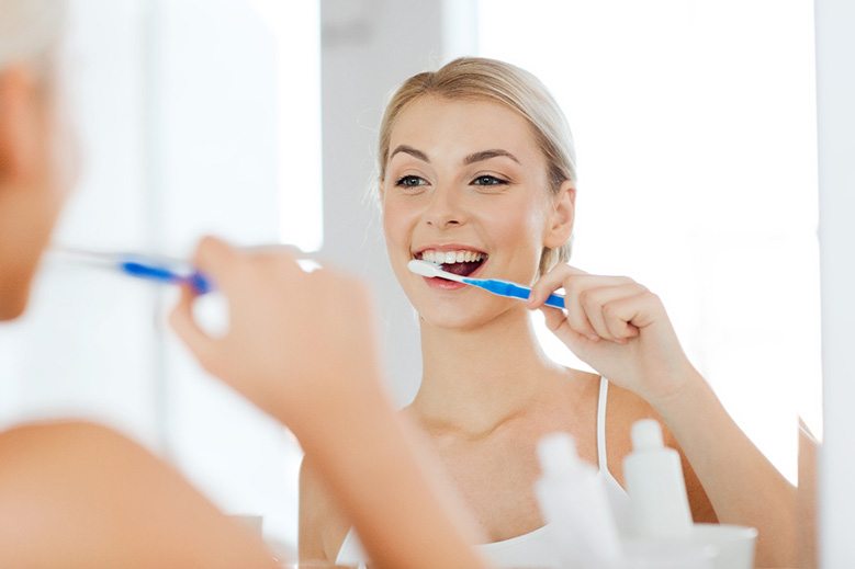 young woman brushing teeth in bathroom mirror