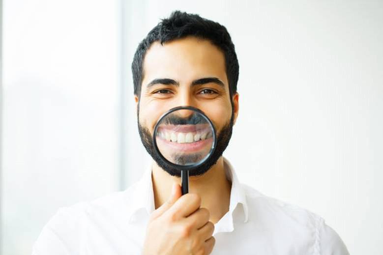 man holding a magnifying glass to his smile